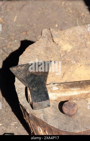 Die Axt liegt auf einem Holzdeck. Als Nächstes ist ein Hammerbock zum Nieten einer Sense. Stockfoto