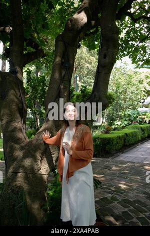 Eine Frau steht neben einem großen Baum und berührt seinen Stamm, mit üppig grünem Laub im Hintergrund. Stockfoto