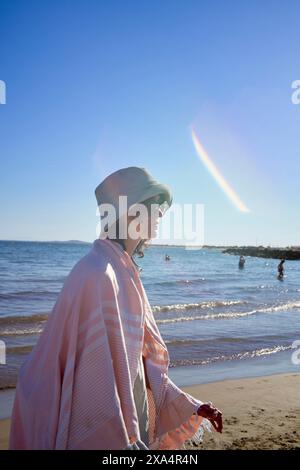 Eine Person schlendert am Strand entlang mit einem hellen Sonnenlicht, das am klaren blauen Himmel zu sehen ist. Stockfoto