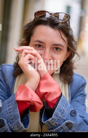 Lächelnde Frau mit Sonnenbrille auf dem Kopf, die sich lässig auf einer Stadtstraße posiert. Stockfoto