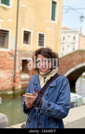 Lächelnde Frau mit Smartphone, die vor einem Kanal in Venedig steht. Stockfoto