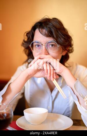 Frau mit Gläsern, die das Kinn auf den Händen liegen, an einem Restauranttisch mit einer Tasse Tee. Stockfoto