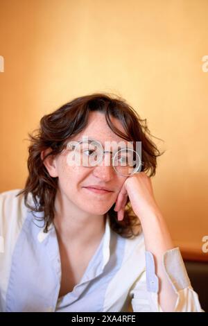 Lächelnde Frau mit einer Brille, die ihr Kinn auf der Hand vor einem warmen Hintergrund auflegt. Stockfoto