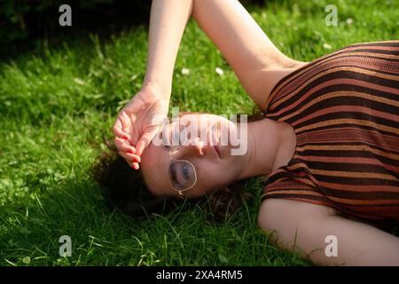 Frau, die sich im Sonnenlicht auf dem Gras mit einer Brille entspannt Stockfoto