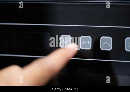 Nahaufnahme einer Person, die die Taste nach unten auf einem digitalen Bedienfeld mit einem Display, das die Einstellungen für Feuchtigkeit und Temperatur anzeigt, drückt. Stockfoto