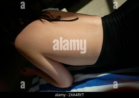 Nahaufnahme der sonnenbestrahlten Schulter und des Rückens einer Person mit Wassertropfen auf der Haut. Stockfoto