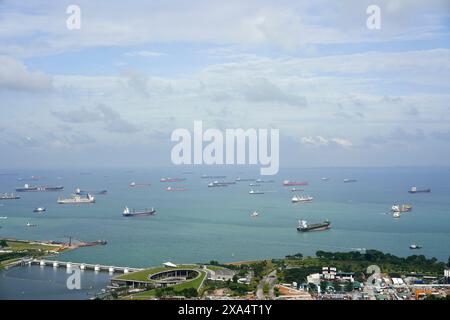 Aus der Vogelperspektive auf eine belebte Schifffahrtsstraße mit zahlreichen Frachtschiffen in der Nähe einer Küstenstadt an einem bewölkten Tag. Stockfoto