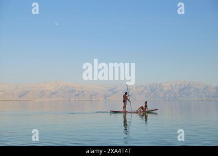 Zwei Personen paddeln auf einem ruhigen See mit fernen Bergen unter klarem Himmel. Stockfoto