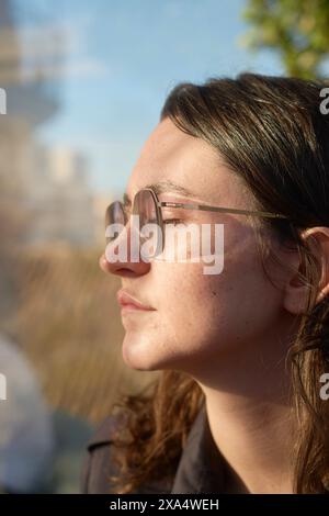 Seitenprofil einer jungen Frau mit Brille, die den Sonnenschein mit geschlossenen Augen genießt. Stockfoto