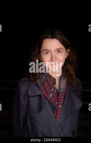 Lächelnde Frau mit lockigem Haar, grauem Mantel und gemustertem Schal vor dunklem Hintergrund. Stockfoto