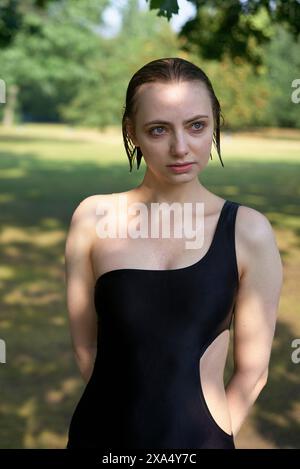 Selbstbewusste Frau in einem schwarzen Kleid steht draußen mit nassem Haar und einem konzentrierten Ausdruck. Stockfoto