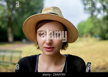 Frau mit Strohhut und schwarzer Spitze lächelt in einem Park mit grünen Bäumen im Hintergrund. Stockfoto