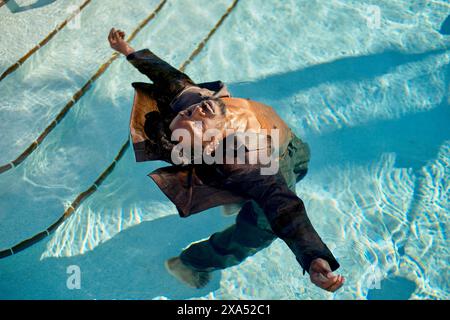 Mann schwimmt friedlich in einem klaren blauen Pool, mit Sonnenlicht, das durch das Wasser reflektiert. Stockfoto