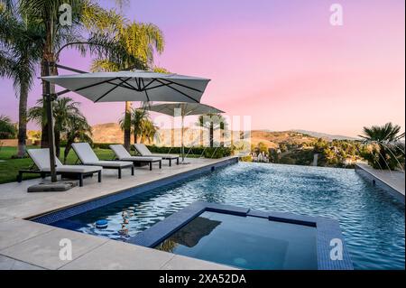 Blick auf den Sonnenuntergang auf einen ruhigen Pool mit Liegestühlen und Sonnenschirmen Stockfoto