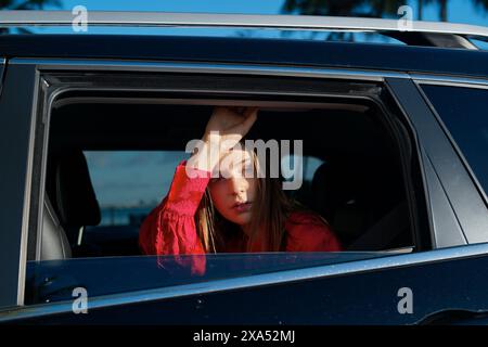 Frau in einer roten Jacke, die während des Sonnenuntergangs aus einem Autofenster blickt. Stockfoto