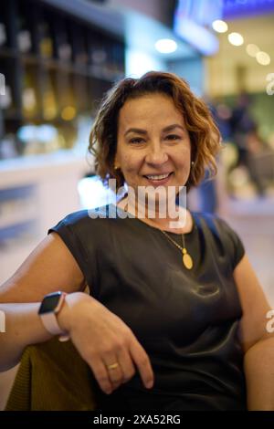 Eine Frau in schwarzem Lederkleid, die auf einer Café-Bank sitzt Stockfoto
