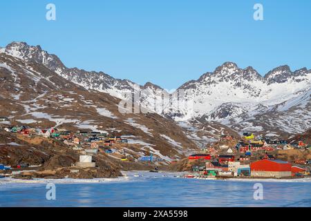 Südöstliches Grönland, Region Ammassalik. Typische farbenfrohe Häuser in der abgelegenen Gemeinde Tasiilaq. Malerische Aussicht auf das schnelle Eis im Frühling. Nur redaktionell. Stockfoto