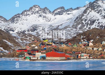 Südöstliches Grönland, Region Ammassalik. Typische farbenfrohe Häuser in der abgelegenen Gemeinde Tasiilaq. Malerische Aussicht auf das schnelle Eis im Frühling. Nur redaktionell. Stockfoto