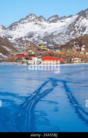 Südöstliches Grönland, Region Ammassalik. Typische farbenfrohe Häuser in der abgelegenen Gemeinde Tasiilaq. Malerische Aussicht auf das schnelle Eis im Frühling. Nur redaktionell. Stockfoto