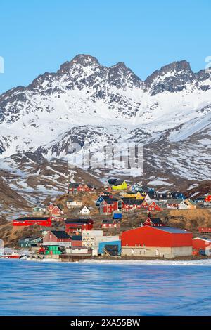 Südöstliches Grönland, Region Ammassalik. Typische farbenfrohe Häuser in der abgelegenen Gemeinde Tasiilaq. Malerische Aussicht auf das schnelle Eis im Frühling. Nur redaktionell. Stockfoto