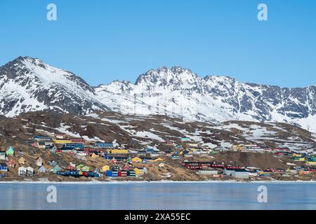 Südöstliches Grönland, Region Ammassalik. Typische farbenfrohe Häuser in der abgelegenen Gemeinde Tasiilaq. Malerische Aussicht auf das schnelle Eis im Frühling. Nur redaktionell. Stockfoto