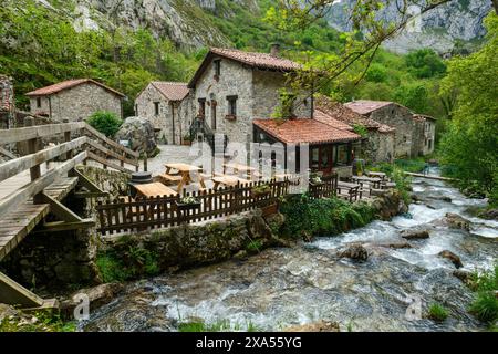 Ein kleines Dorf, durch das ein Fluss fließt. Die Häuser sind aus Stein und haben eine rustikale Atmosphäre. Es gibt mehrere Bänke und Tische draußen, ein Stockfoto