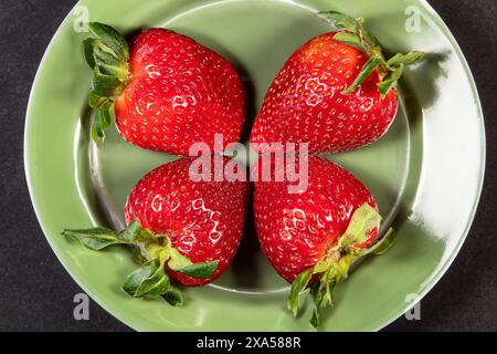 Ein Blick von oben auf vier reife Erdbeeren auf einem grünen Teller Stockfoto