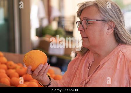 Eine ältere weißhaarige Frau, die Orangen auf einem Straßenmarkt kauft Stockfoto