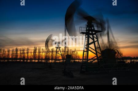 Die Ölpumpen sind im Hintergrund mit einer untergehenden Sonne versehen. Stockfoto