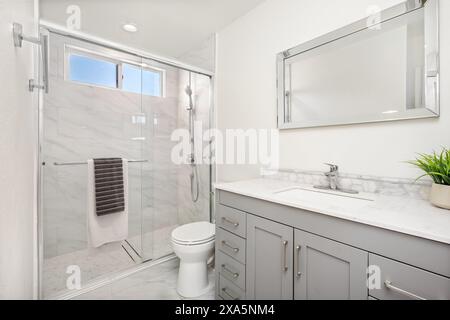 Dieses Bild zeigt ein modernes Badezimmer mit neutraler Farbpalette. Das Badezimmer verfügt über eine Duschkabine aus Glas mit einem Handtuch, das an einem Chrom hängt. Stockfoto
