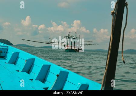 Ein Fischerboot wird auf ruhigen Meeresgewässern unter einem bewölkten Himmel vom Bug eines blauen Bootes aus gesehen und zeigt einen ehrlichen Moment des täglichen Lebens und des Lebensunterhalts in Th Stockfoto