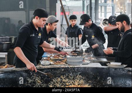 Männliche Köche legen fertige traditionelle usbekische Pilaw aus einem Kessel auf Teller im zentralasiatischen Pilaw Center Besh Qozon. Taschkent, Usbekistan - 16. April 2024 Stockfoto
