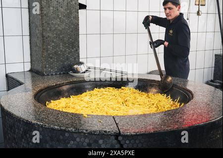 Männliche Köche kochen gelbe Karotten in einem Kessel für traditionelle usbekische Pilaw im zentralasiatischen Pilaw-Zentrum Besh Qozon. Taschkent, Usbekistan - 16. April 2024 Stockfoto