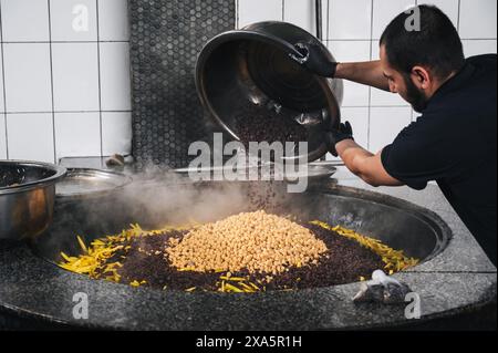 Der männliche Koch fügt Berberitze in einen Kessel mit Karotten und Kichererbsen ein, um usbekische Pilaw im zentralasiatischen Pilaf-Zentrum Besh Qozon zu kochen. Taschkent, Usbekistan - 16. April 2024 Stockfoto