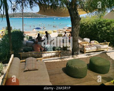 Eine Gruppe von Leuten, die sich an einem Strand mit großen Stühlen in Porto Taverna, Italien, entspannen Stockfoto