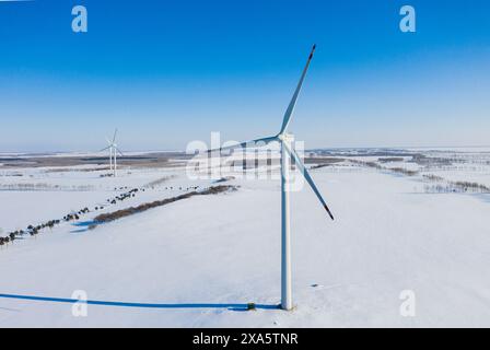 Eine Windkraftanlage auf einem schneebedeckten Feld unter klarem blauem Himmel Stockfoto