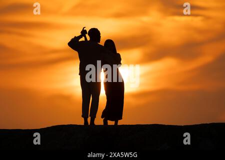 Ein Paar, das bei Sonnenuntergang auf einem Hügel steht und die Frau den Mann umarmt Stockfoto