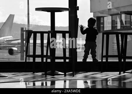 Flughafen Nizza Côte d'azur, Frankreich, 21. Mai 2024: Silhouette von Kleinkindern, die Flugzeuge am Flughafenterminal beobachten, in Schwarz-weiß Stockfoto