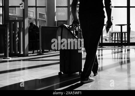 Flughafen Nizza Côte d'azur, Frankreich, 21. Mai 2024: Die untere Hälfte des Mannes geht mit rollendem Koffer im Flughafenterminal in Schwarz-weiß Stockfoto