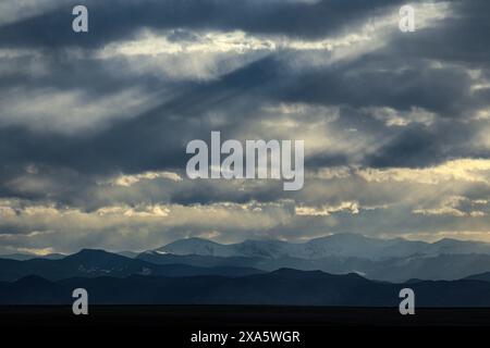 Die Berge unter einem bewölkten Himmel mit Sonnenstrahlen, die durch dunkle Wolken hindurch ragen. Stockfoto