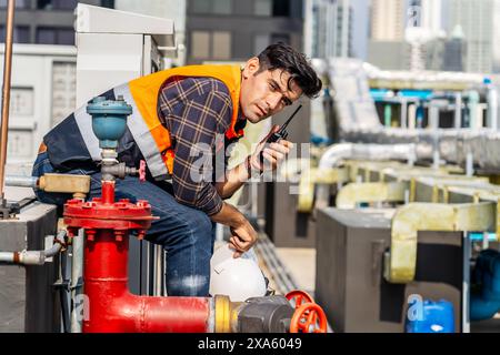 Ein technischer Vorarbeiter, der eine Pause einlegt und im Funk über die Wartung von Gebäudesystemen in Thailand, Bangkok, plaudert Stockfoto