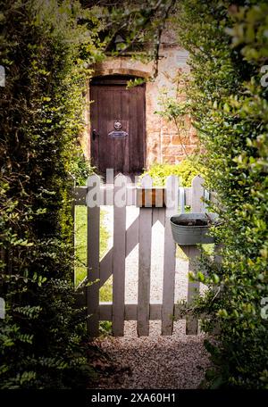 Ein Holztor vor einem kleinen gemütlichen Haus mit grünem Garten Stockfoto