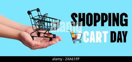 Weibliche Hände, die einen kleinen Einkaufswagen auf blauem Hintergrund halten. Banner für den Tag des Warenkorbs Stockfoto
