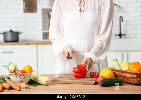 Schwangere Frau, die frisches Gemüse auf hölzernem Küchentisch schneidet Stockfoto
