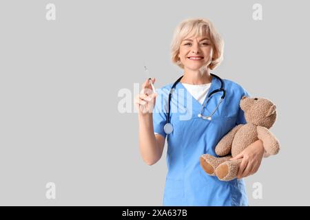 Kinderärztin mit Spielzeugbär und Impfstoff auf hellem Hintergrund Stockfoto