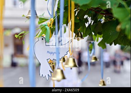 LEMBERG, UKRAINE – 04. JUNI, 2024: Eine Weißpapiertaube mit der Inschrift „Mariupol“ und Glocken, die von den Teilnehmern der Kampagne „Children’s Voices“ auf dem Ploschcha Anheliv Platz in der Nähe der Garnisonkirche der Heiligen Apostel Peter und Paul der UGCC am Tag des Gedenkens an Kinder, die an einen Baum gebunden wurden starb infolge der bewaffneten Aggression der Russischen Föderation gegen die Ukraine, Lemberg, Westukraine Stockfoto