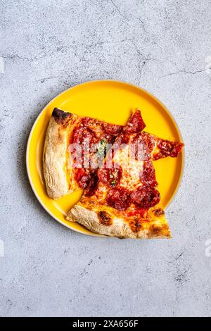 Pepperoni Pizza-Scheiben auf gelbem Teller auf grauem Hintergrund Stockfoto