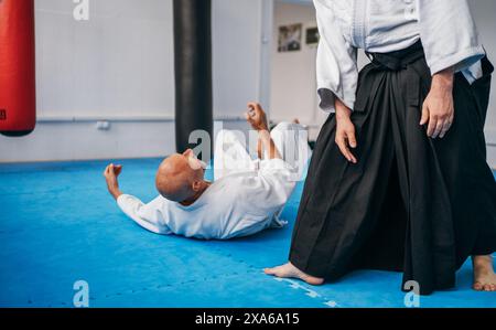 Zwei Männer üben Aikido im Dojo mit traditionellen weißen Kimono und Hakama. Ein Mann führt eine präzise Technik aus, um seinen Partner dazu zu führen, Dämonen zu mattieren Stockfoto