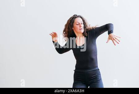 Frau in schwarzem Outfit lacht fröhlich, während sie lockiges Haar über ihre Schultern tanzt. Ausdrucksstarke Bewegungen und ein strahlendes Lächeln halten den Moment fest Stockfoto