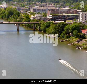 Ein weißes Boot, das entlang eines Flusses an Gebäuden und einer Brücke in der Innenstadt von Augusta, Georgia, in der Nähe des Savanna River fährt Stockfoto